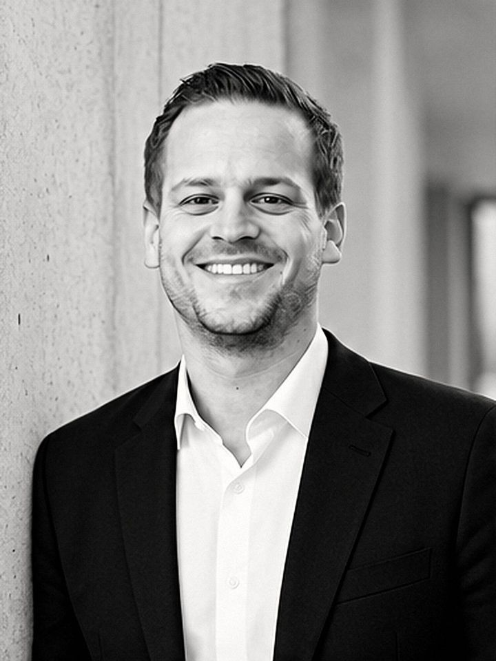 Porträt von Dominik Gerber, Geschäftsführer von surge, in Anzug und weißem Hemd vor einer Betonwand