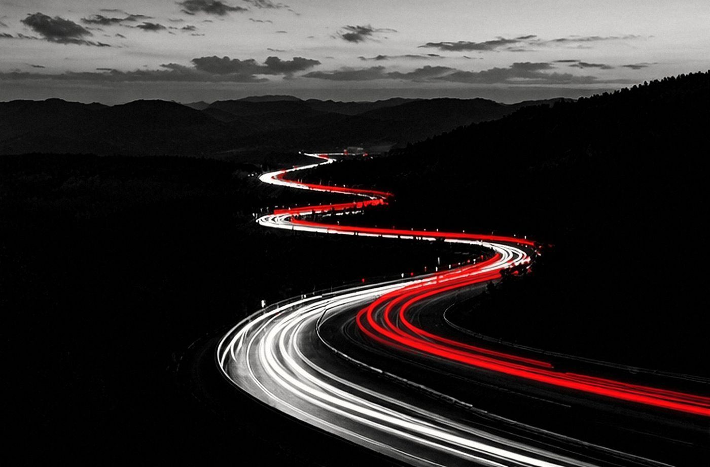 Serpentine durch bewaldete Hügel bei Nacht, eine rote Lichtspur zieht nach oben